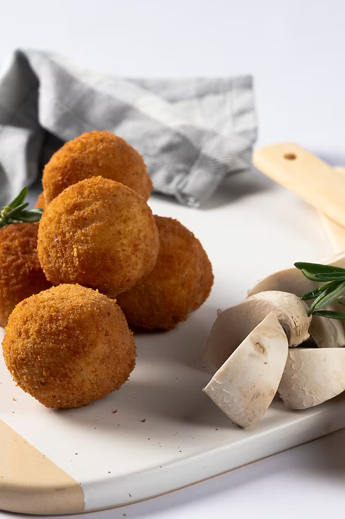 Breaded round food items on a white plate with mushrooms and rosemary.